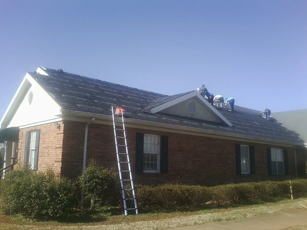 Crew tearing shingles off a brick ranch roof with a ladder set — Emergency Roof Repair work by our crew in Mechanicville