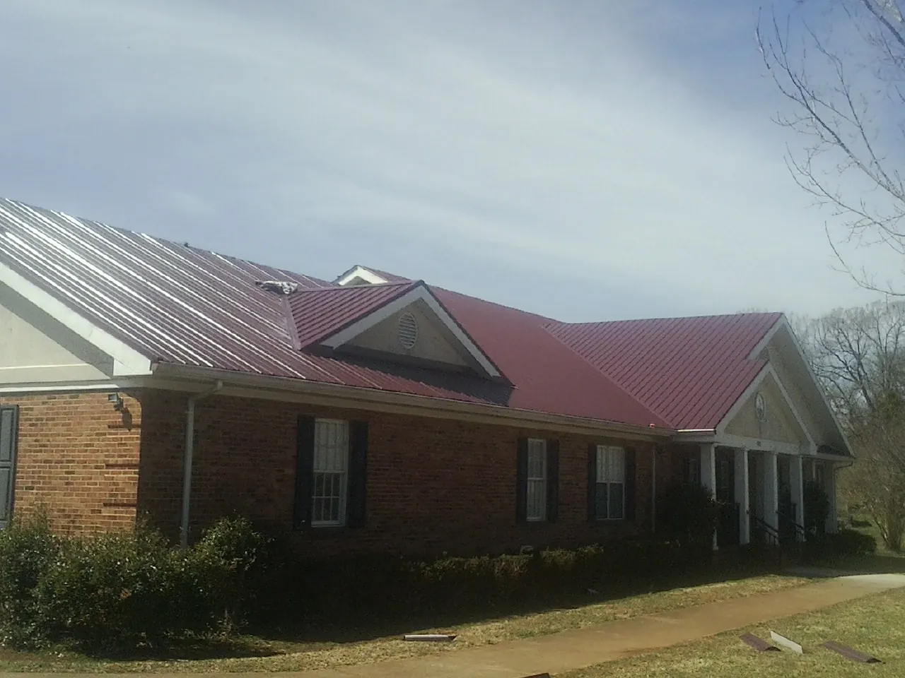 Red metal roof with gabled entries on a long brick building, from a Hail Damage Roof Repair job in Mechanicville