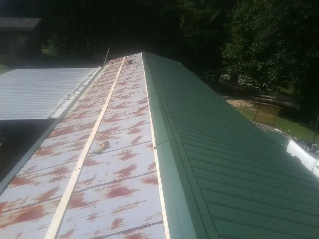 Old rusted panels beside newly installed green metal roofing in Mechanicville
