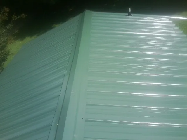 New green metal panels meeting at the ridge of a roof — Flat Roof Repair work by our crew in Mechanicville