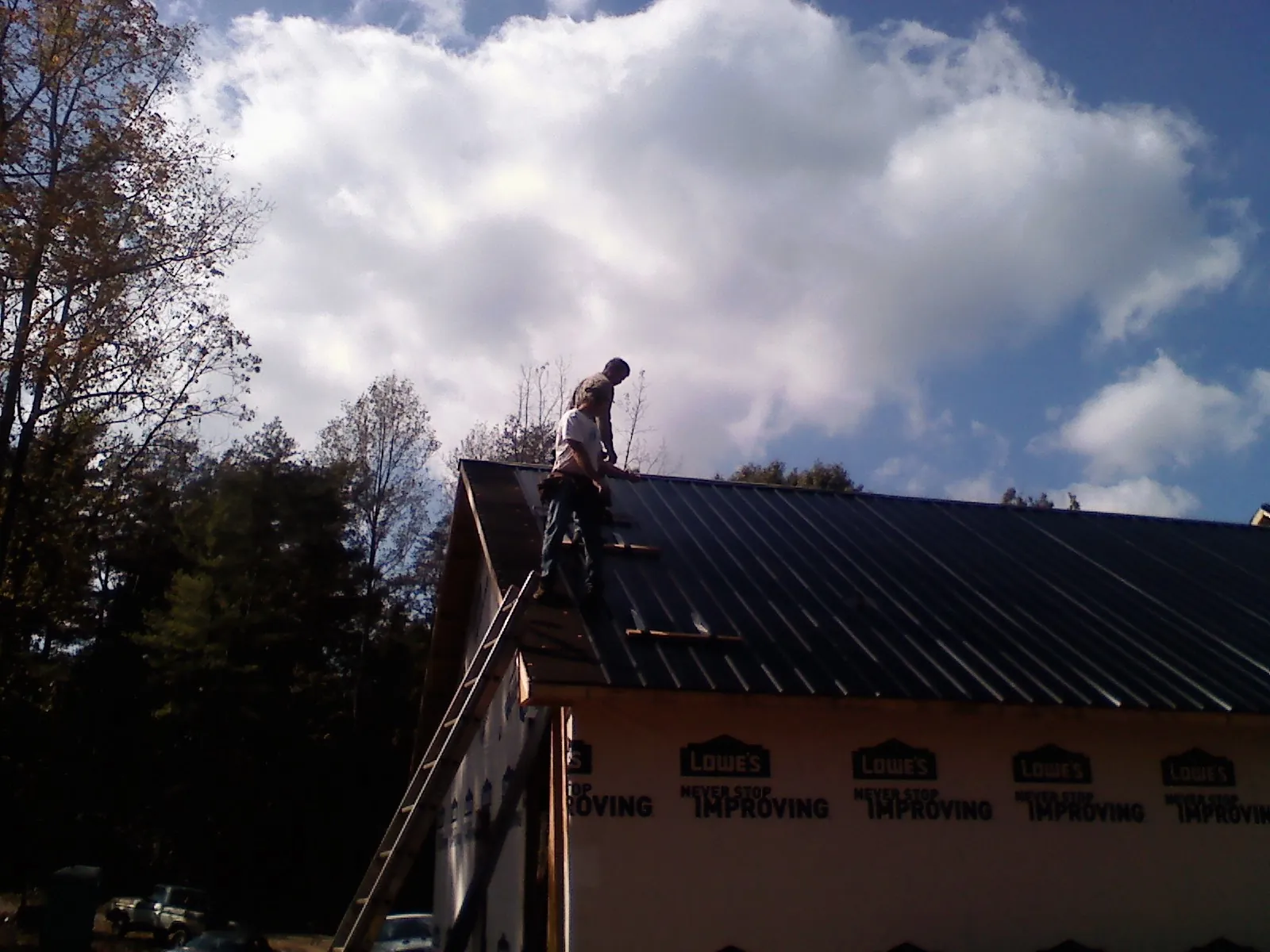 Roofer fastening dark metal panels high against a cloudy sky, from a Roof Inspection job in Mechanicville