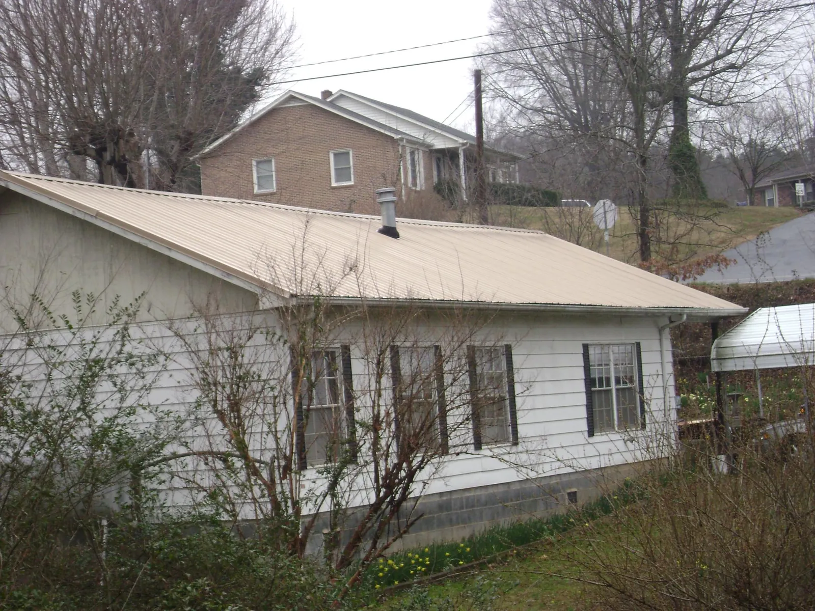 Tan metal roof on a white sided house set into a hillside — Commercial Roofing by Roofing Brothers in Mechanicville